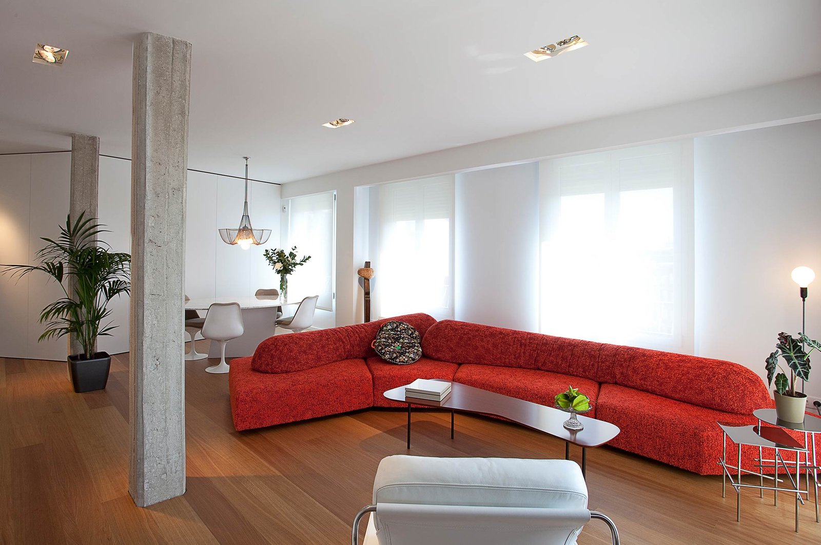 Decoración comedor Madrid amplio apartamento moderno con gran sofá rojo suelo parquet y pilares hormigón