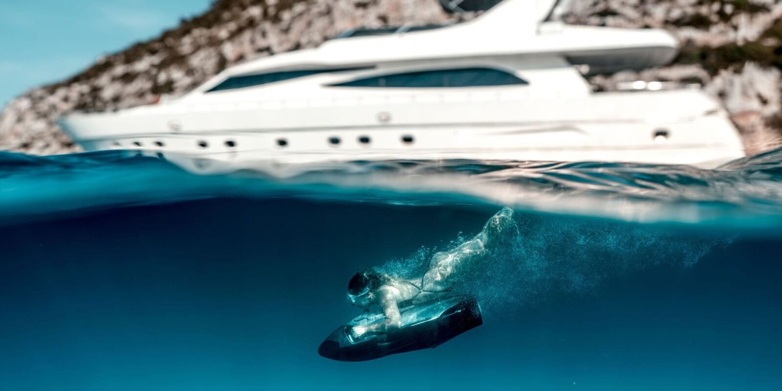 Vemos un yate de lujo junto a una persona que practica submarinismo en las aguas turquesas de una cala de Formentera.